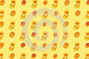 Creative pattern made with sliced blood orange and glass with lemonade or water on yellow background. Summer fruit and refreshment