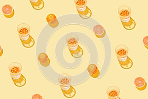 Creative pattern made with sliced grapefruit, blood orange and glass with lemonade or water on yellow background. Summer fruit and