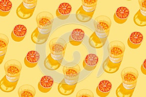Creative pattern made with sliced grapefruit, blood orange and glass with lemonade or water on yellow background. Summer fruit and