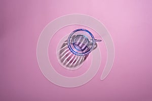 Creative photo with a blue glass cup with beautiful reflective shadows on a pink background, top view with space under