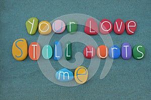 Your love still hurts me, phrase composed with multi colored stone letters over green sand