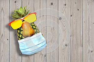 Creative Pineapples in sunglasses and medical mask on wooden background