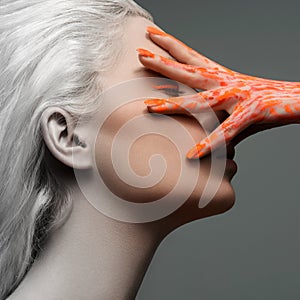 Creative portrait of a beautiful girl with hand on face, white hair. The hand is painted with orange paint.