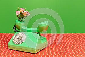 Creative portrait with telephone receiver and flowers inside on festive red table over green studio background. Spring