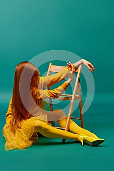 Creative portrait of unknown redhead girl with long straight silky hair posing on armchair, sitting in strange poses