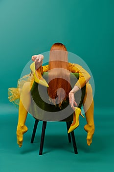 Creative portrait of unknown redhead girl with long straight silky hair posing on armchair, sitting in strange poses