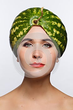 Creative portrait of a woman with a watermelon on her head instead of a hat. White background