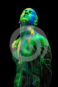Creative portrait of young man standing with closed eyes. Multi-colored paints, dyes flow down his head, shoulders and