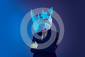 Creative portrait of young stylish man in business suit with cardboard mask on his head isolated on dark blue studio