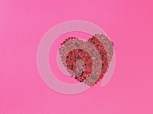 A creative red heart made of many small hearts on a pink background. The concept of Valentine`s Day