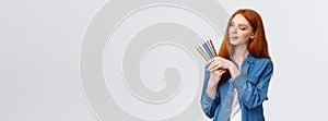 Creative and skilful good-looking redhead female in denim shirt, picking colored pencils, smiling thinking what draw