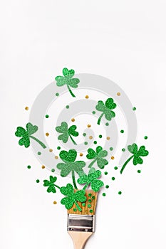 Creative St. Patricks Day greeting card. Paint brush with green glitter shamrocks and confetti. Minimal St. Patricks Day greeting