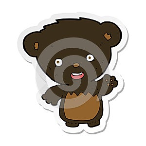 A creative sticker of a cartoon black bearcub waving