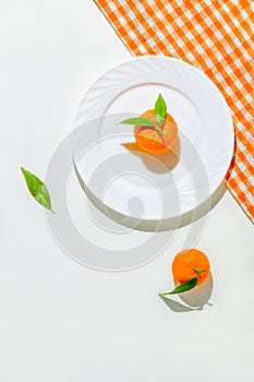 Creative still life composition made of fresh orange mandarin fruits on a plate on white background with cage kitchen towel.