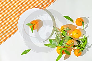 Creative still life composition made of fresh orange mandarin fruits on white background with cage kitchen towel and a plate.