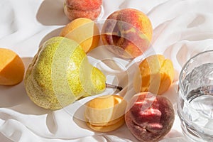 Creative still life composition made of fruits closeup and a glass of water on white fabric background. Summer refreshment and