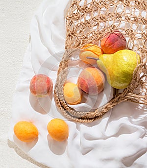 Creative still life composition made of fruits mesh bag on white fabric background. Summer refreshment and freshness concept