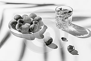 Creative still life composition made of glass with lemonad and lychee fruits on white background with palm tree leaf shadow.