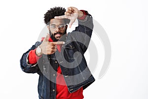 Creative and stylish african-american male artist in glasses, denim jacket over red hoodie raising hands near face as