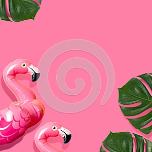 Creative summer beach concept. Inflatable pink mini flamingo and tropical leaf monstera on pink background, pool float party. Flat