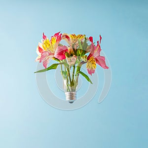 A creative summer concept with a broken light bulb in which flowers grow on a light blue background. Minimal style.