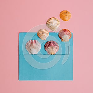 Creative summer flat lay with colorful sea shells, coming out of blue envelope. Minimal compositon on pastel pink background