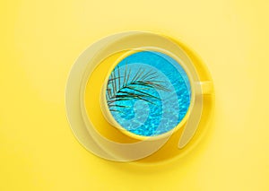 Creative summer minimal art poster. Yellow coffee cup with blue water and palm leaf on yellow background. Art collage. Top view