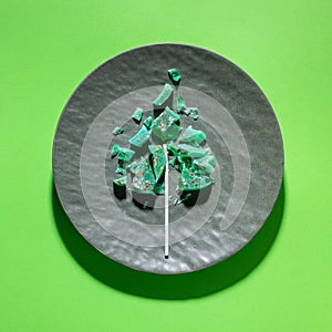 Creative sweet Christmas tree made of pieces of fractured green lollipop on grey plate on green.