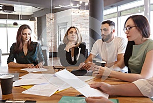 Creative team of four diverse pensive young business people gathered for weekly meeting in office