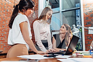 Creative team working on new project together looking and listening to their partner standing around desk using portable