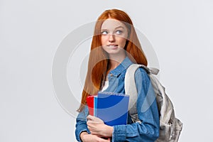 Creative and thoughtful cute daring foxy girl with red hair, hold backpack and notebooks, biting lip looking up