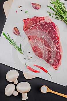 Creative Top view flat lay of fresh raw beef meat striploin steak with rosemary thyme herbs garlic pepper mushrooms on black