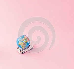 Creative travel concept with a car with a globe on it. Minimal summer composition aganist pastel pink background with copy space.