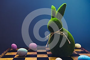 Creative and trendy Easter concept. Easter chess play with colored eggs and Easter green bunny rabbit on the dark blue