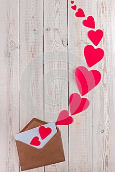 Creative valentine`s day composition, white wooden background with envelope and a lot of big and small red hearts, valentines day