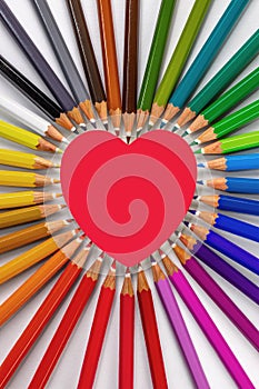 Creative valentines day composition with big red heart surrounded by rainbow-colored pencils on white background, concept of