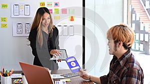 Creative woman holding digital tablet and presenting mobile app interface design to her colleagues.