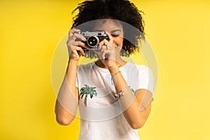 Creative woman-photographer takes photos, isolated on yellow.