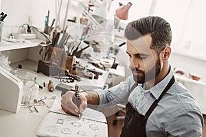 Creative work. Portrait of young bearded jeweler drawing a sketch of a new ring