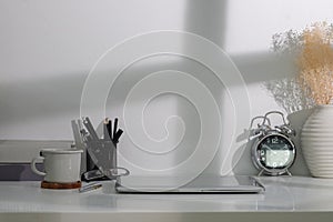 Creative workplace with computer laptop, coffee cup, alarm clock and books on white table