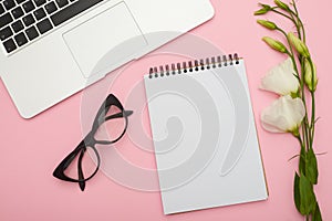 Creative workspace desk with laptop, flowers, jotter and glasses