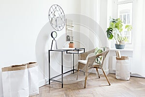 Creative workspace interior in cozy scandinavian apartment with black dest, rattan armchair, plants and office accessories.