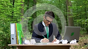 Creative young businessman writing down good ideas at desk in green forest