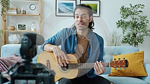 Creative young man guitarist recording video with modern camera playing guitar at home