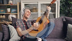 Creative young man is playing the guitar and singing favourite song listening to music in headphones relaxing in modern