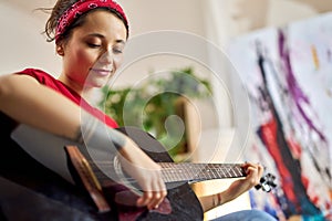 Creative young woman playing acoustic guitar while spending time at home alone