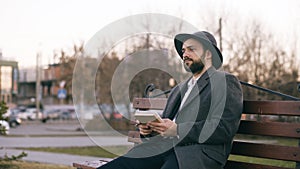 Creative young writer man in hat and coat write notes for his future book with pen in notebook sitting on city street