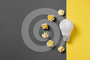 Creativity inspiration, great business idea concept with white light bulb and paper crumpled ball on gray and yellow background.