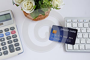 Credit card on computer keyboard with calculator and flowerpot on white desk, with copy space for text. Concept of Online shopping