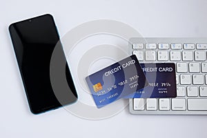 Credit card on computer keyboard with smartphone on white desk. Concept of Online shopping and payment. Top view